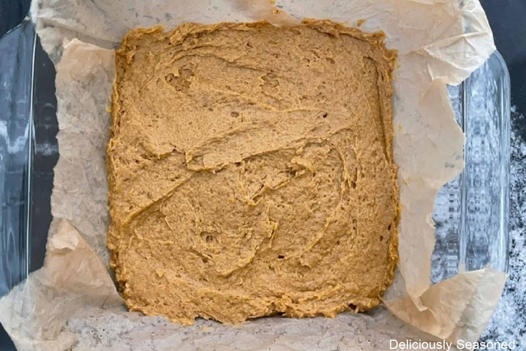 A glass 8 by 8 baking dish with a layer of pumpkin spice coffee cake in it.