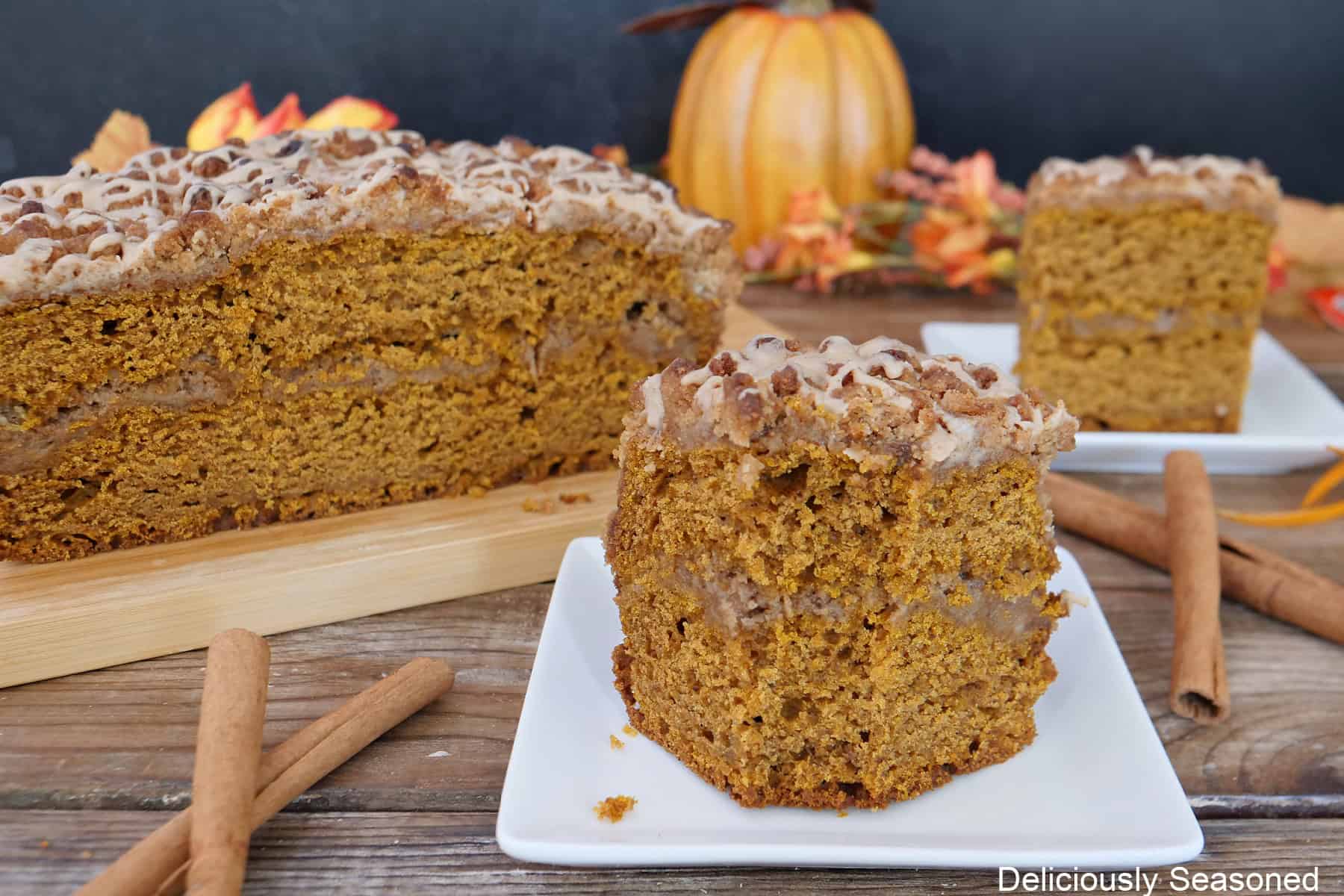 A serving of pumpkin spice coffee cake on a white plate with more coffee cake in the background.