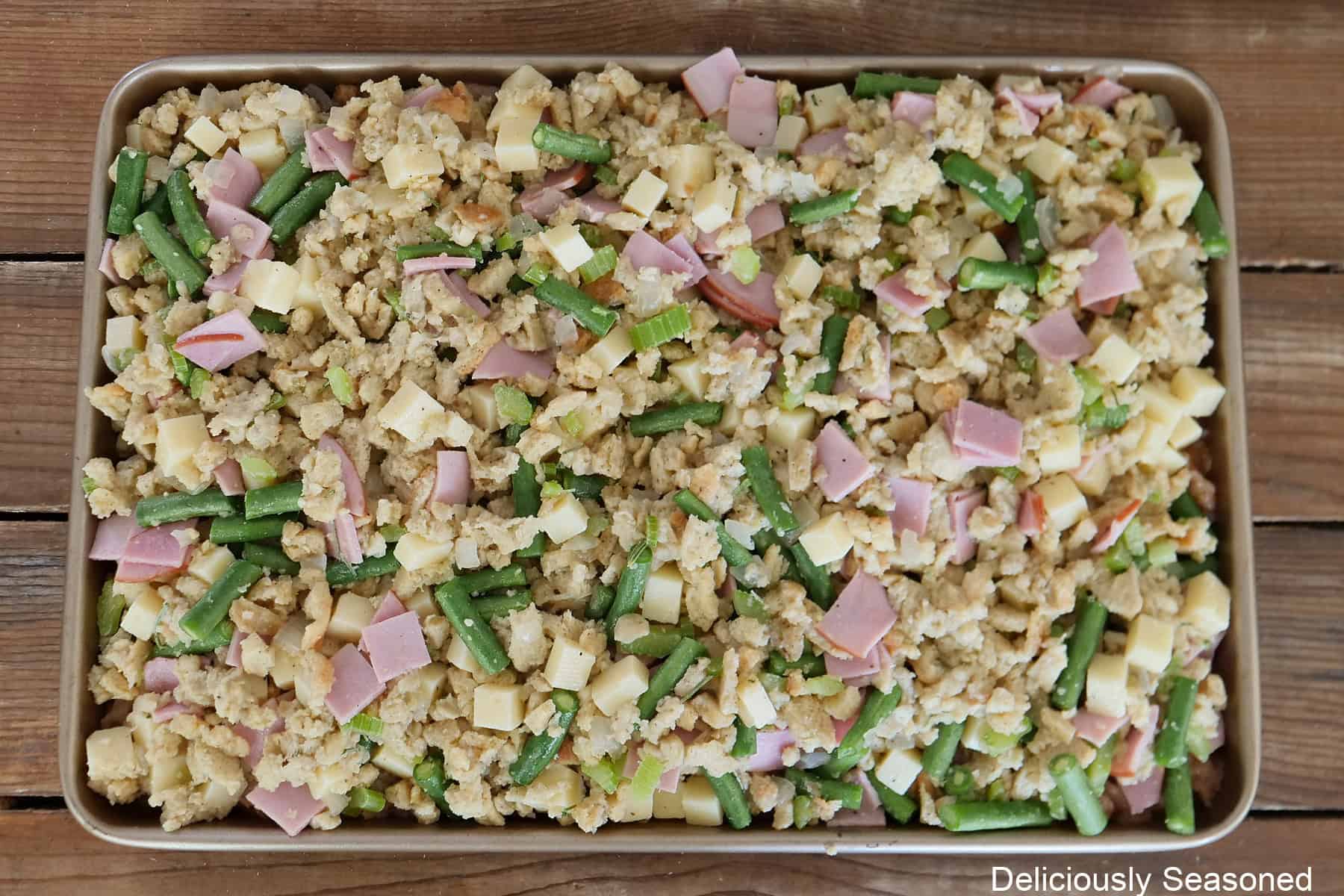 A wood surface with a baking sheet with chicken cordon bleu sheet pan meal on it before being baked in the oven.