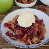 A blue trimmed white bowl with a serving of cranberry apple cobbler with a scoop of vanilla ice cream on top.