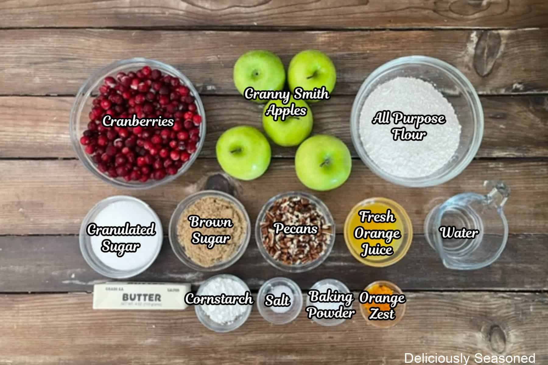 A wood surface with all the ingredients placed on it to make sheet pan cranberry apple cobbler.
