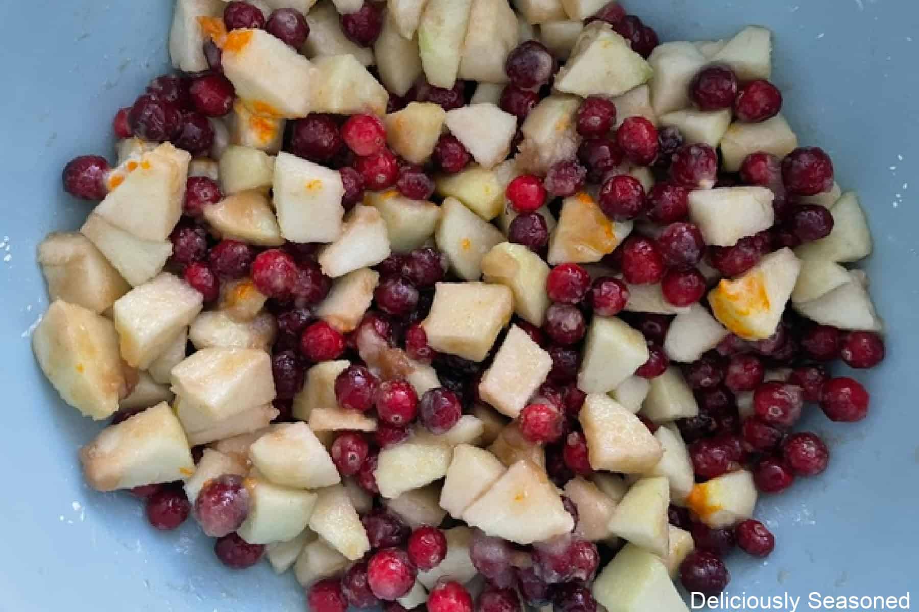 A blue mixing bowl with all the cranberry apple filling ingredients in it.