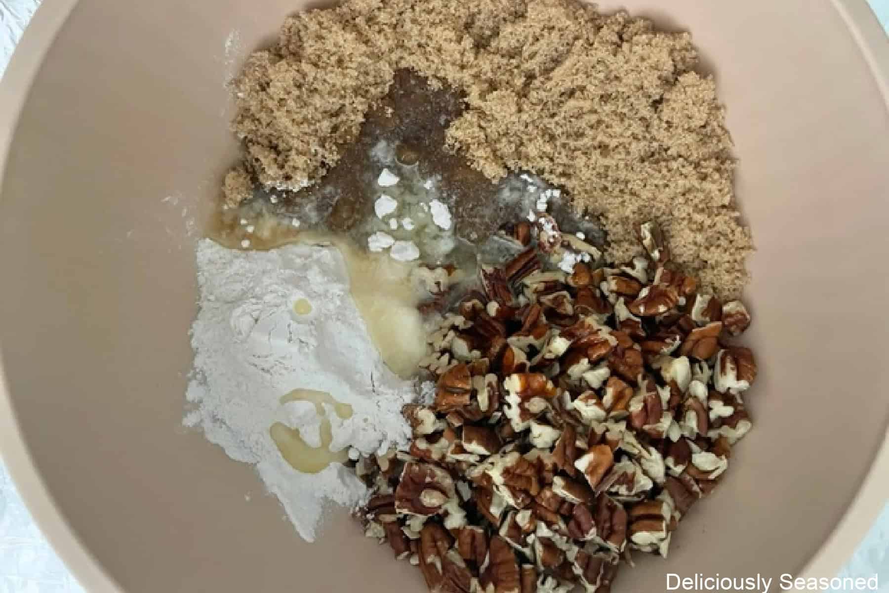 A light colored bowl with chopped pecans, flour, brown sugar, and melted butter in it before being mixed together.