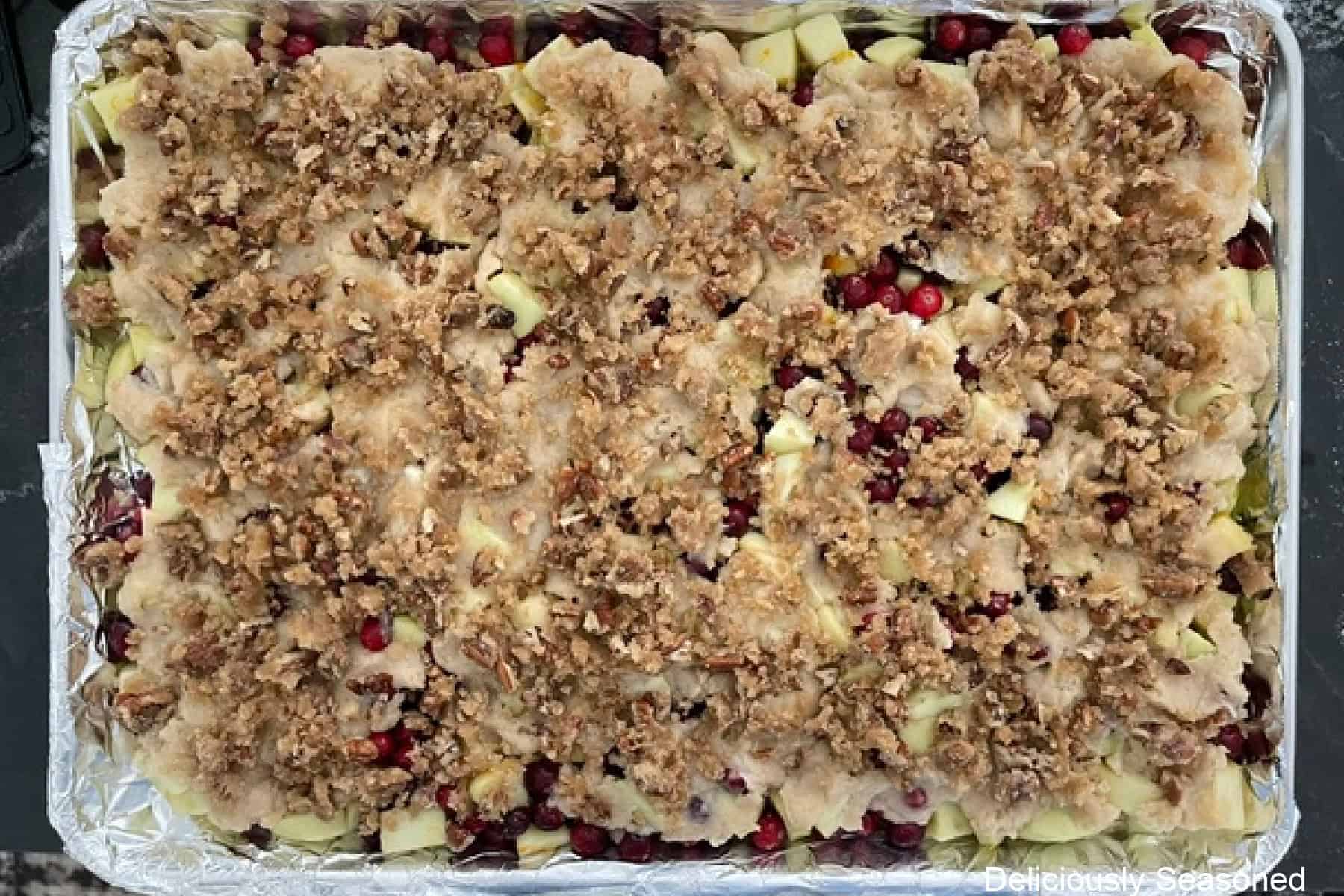 A sheet pan lined with foil with the cranberry apple filling topped with a cobbler topping and then topped with a brown sugar pecan topping before going into the oven.