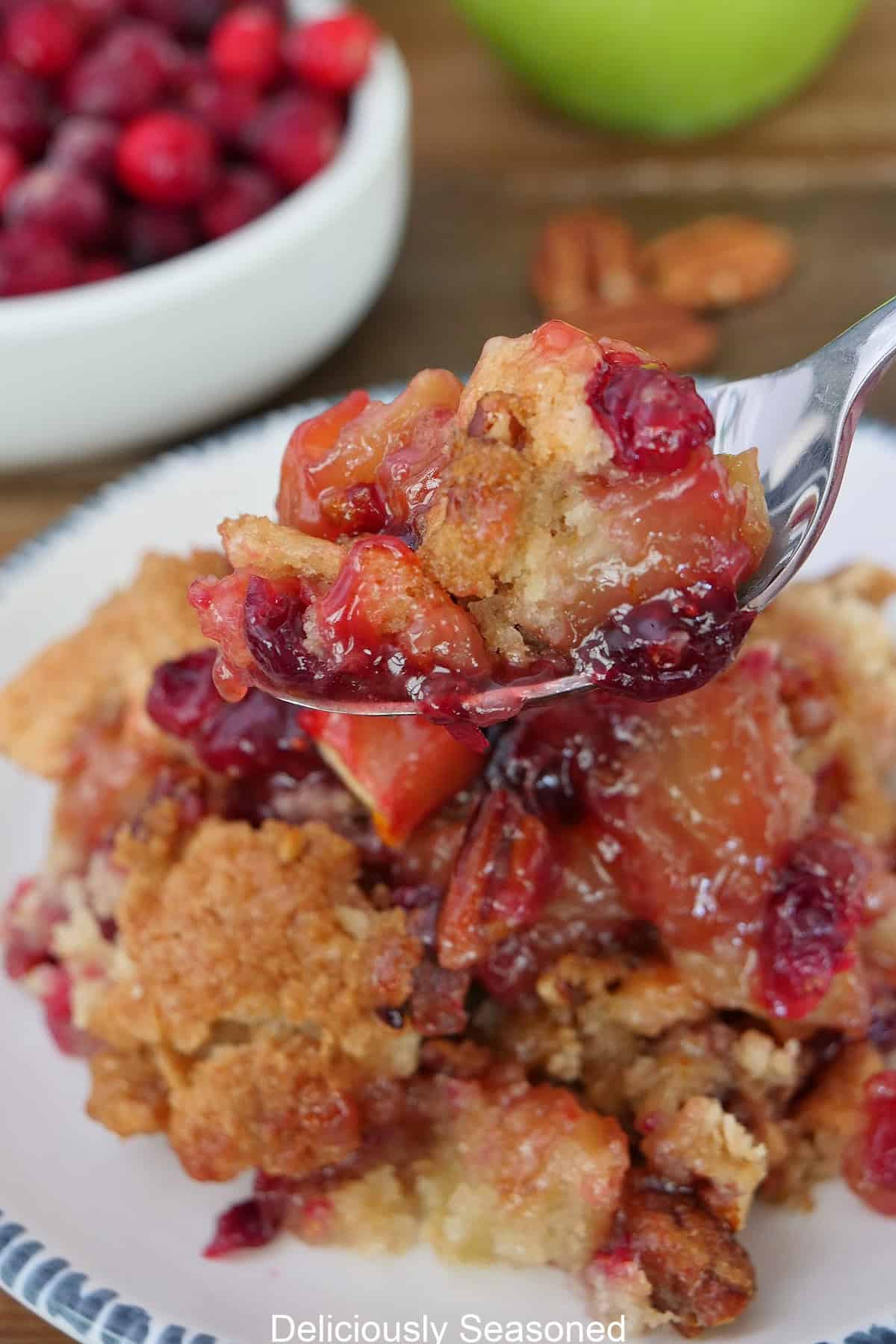 A serving of sheet pan cranberry apple cobbler on a white plate with blue trim and a spoon holding a bite held above the plate.