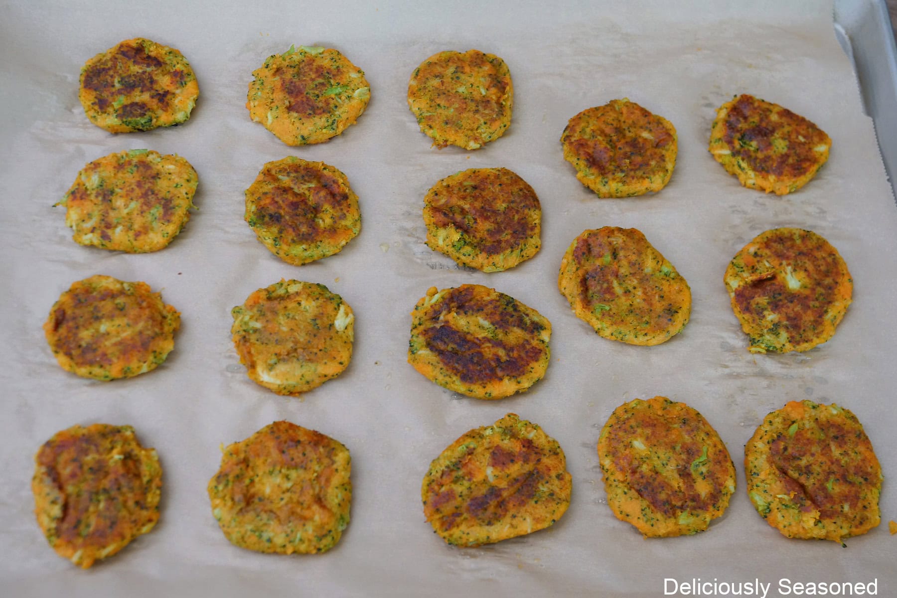 A baking sheet lined with paper towels with eighteen sweet potato broccoli cheddar fritters on it after being fried.