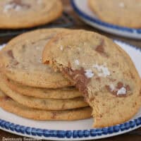 A white plate with blue trim with a stack of four brown butter chocolate bar cookies on it with another cookie leaning on the cookies with a bite out of it.