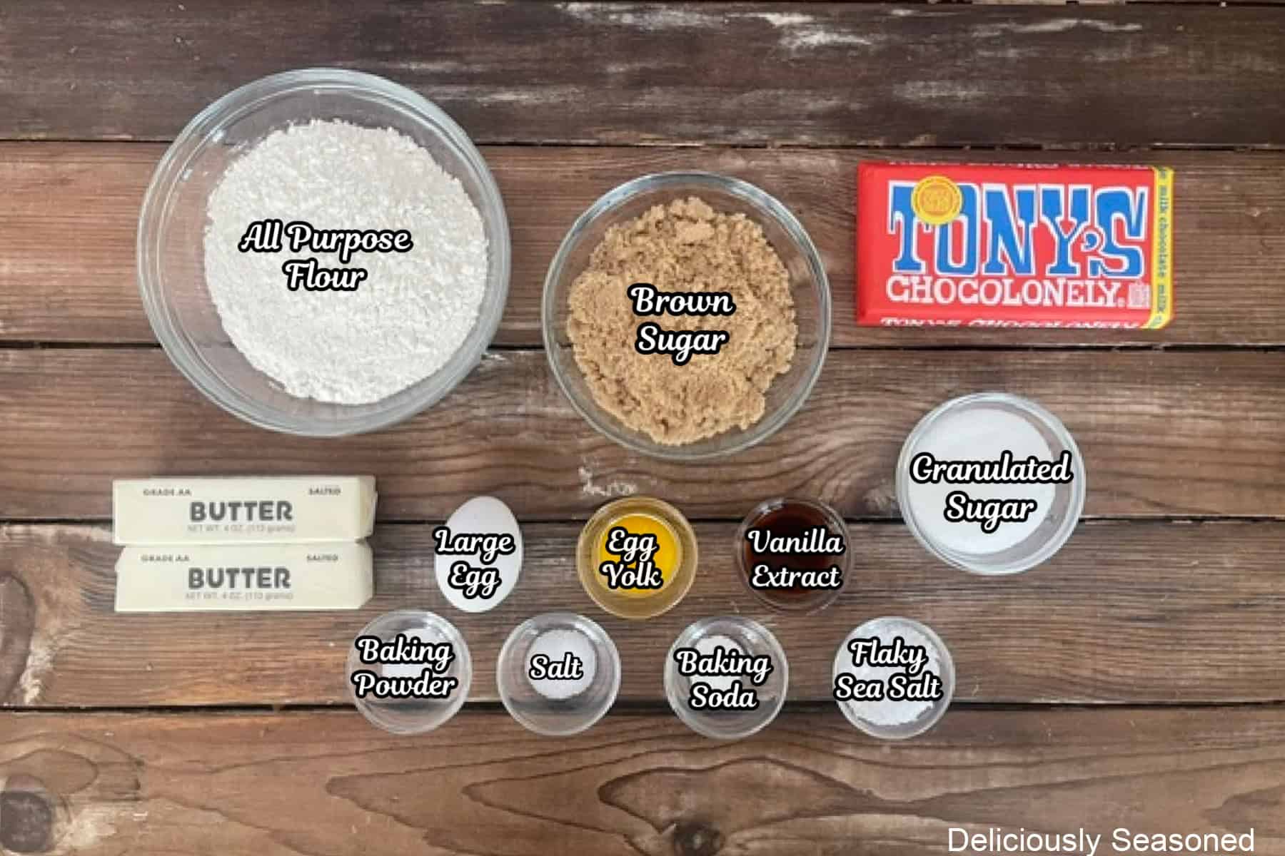 A rustic wood surface with all the ingredients placed on it to make brown butter chocolate bar cookies.