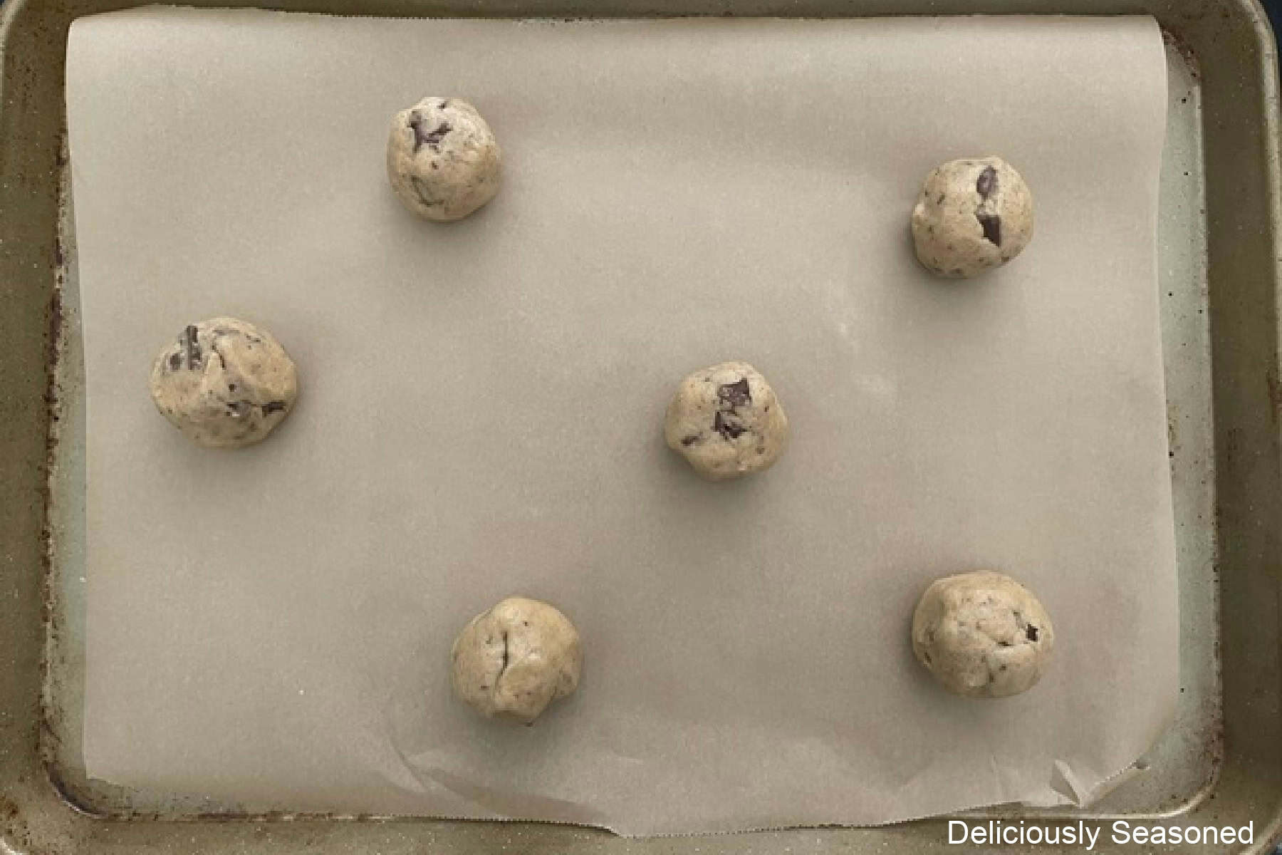 A parchment lined baking sheet with six cookie dough balls on it.