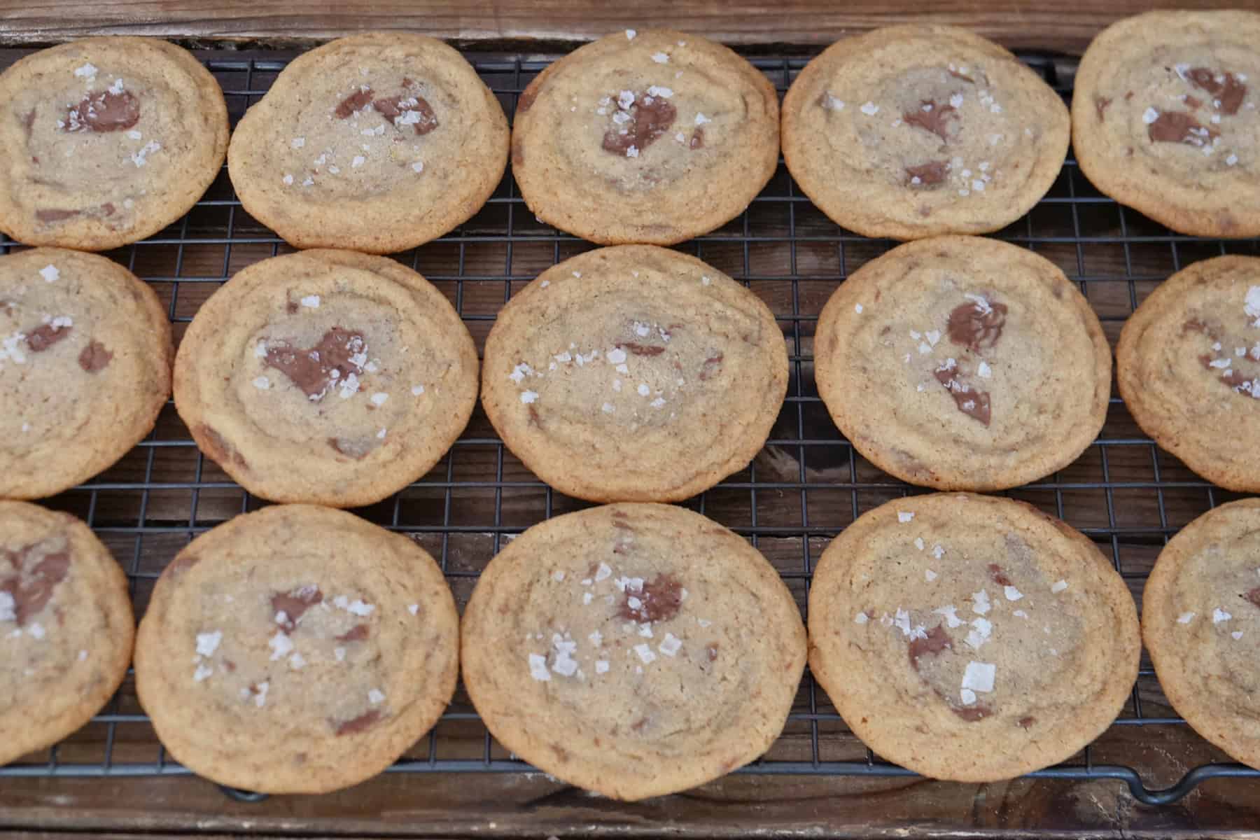 A wire rack with fifteen brown butter chocolate bar cookies on it.