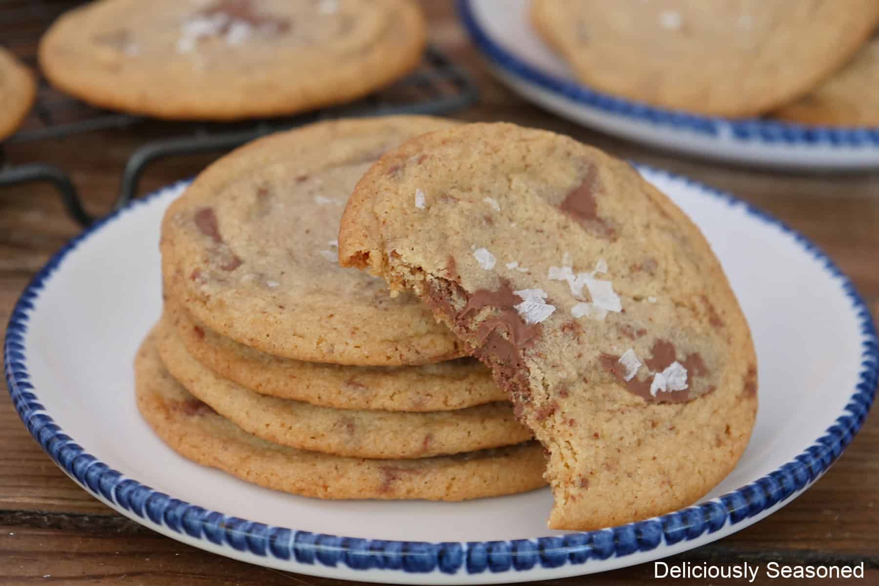 A round white plate with blue trim with a stack of four cookies and one leaning up on the cookies that has a bite taken out of it.