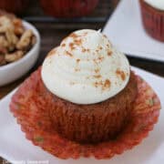 A carrot walnut cupcake with white maple frosting on top placed on a white plate.