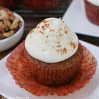 A carrot walnut cupcake with white maple frosting on top placed on a white plate.