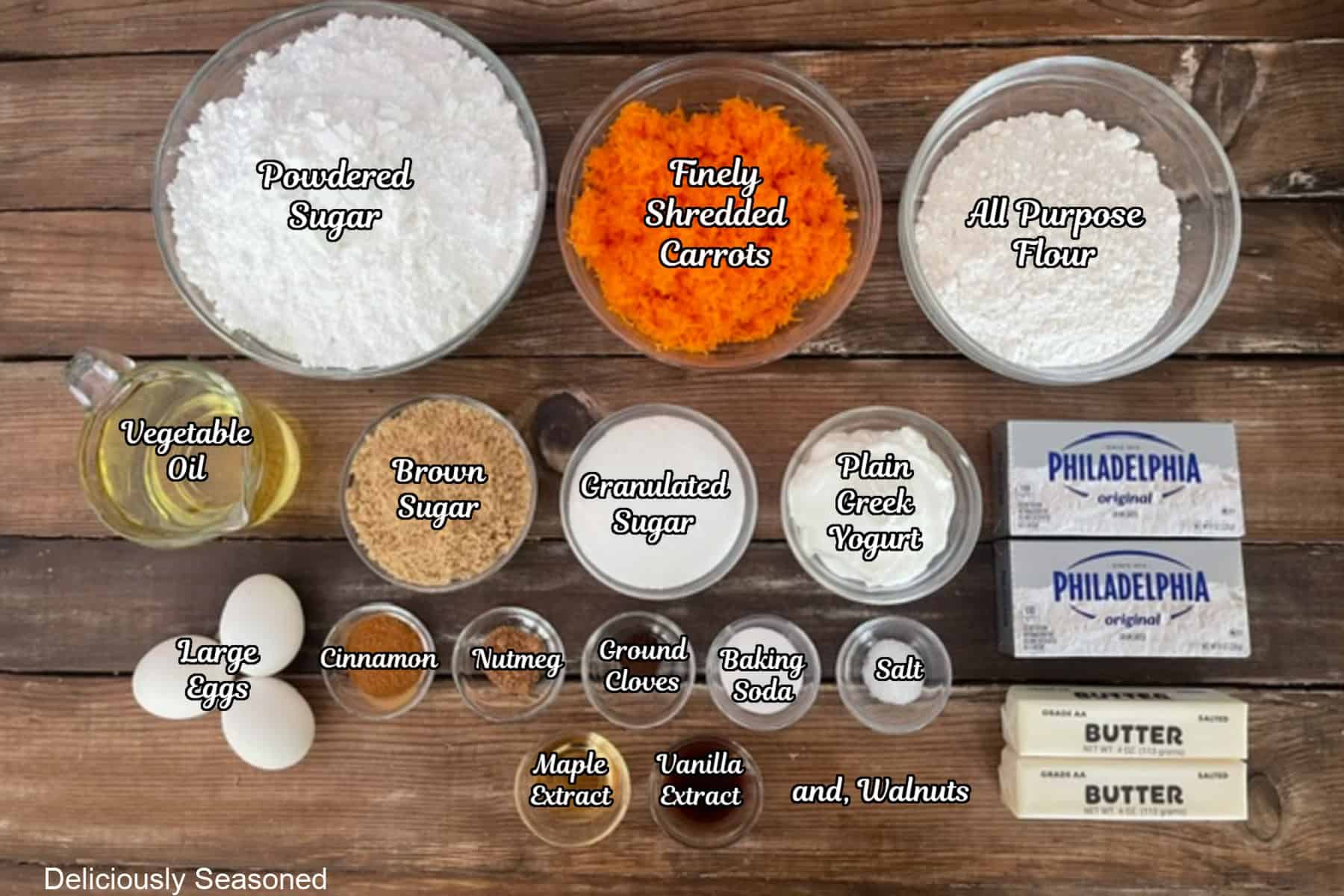 A wood surface with all the ingredients placed on it to make carrot walnut cupcakes with maple frositng.