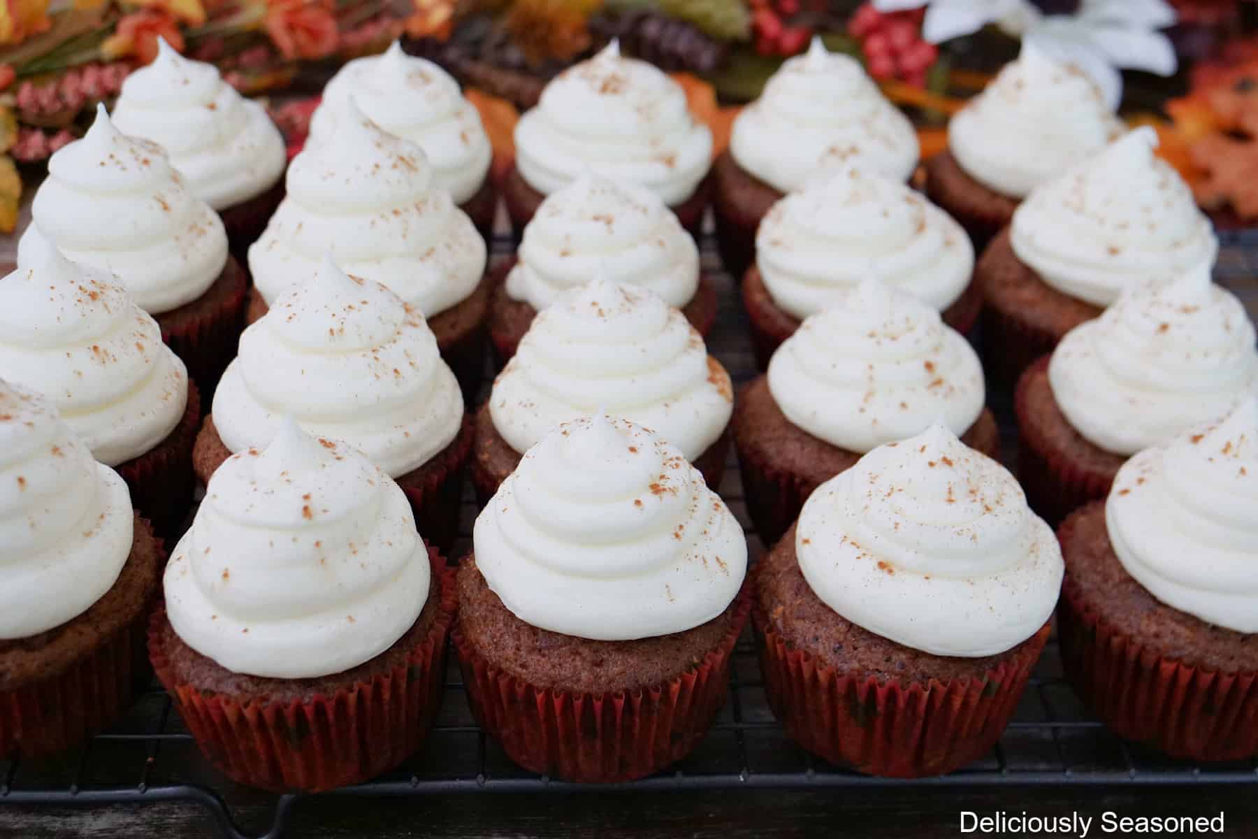 A wire rack with twenty carrot walnut cupcakes with maple frosting on it.