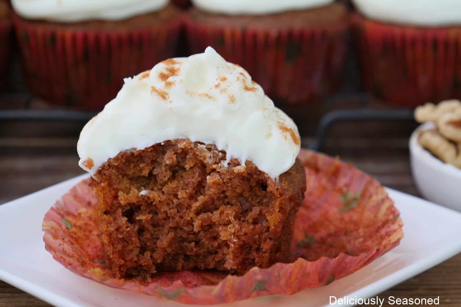 A white plate with a single carrot walnut cupcake with maple frosting on top placed on it.