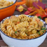 A white bowl filled with a serving of creamy pumpkin sausage pasta with fall foliage in the background.