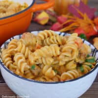 A white bowl filled with a serving of creamy pumpkin sausage pasta with fall foliage in the background.