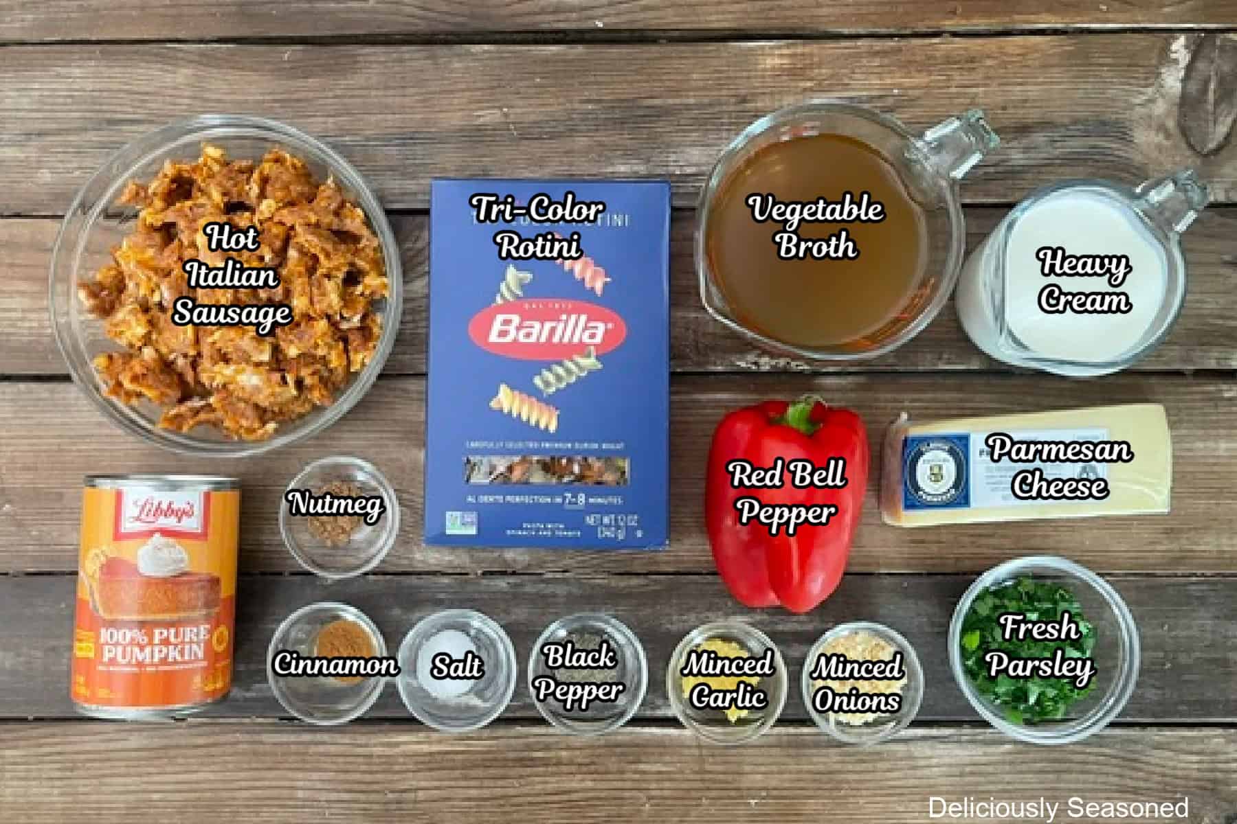 A wood surface with all the ingredients placed on it to make creamy pumpkin sausage pasta.
