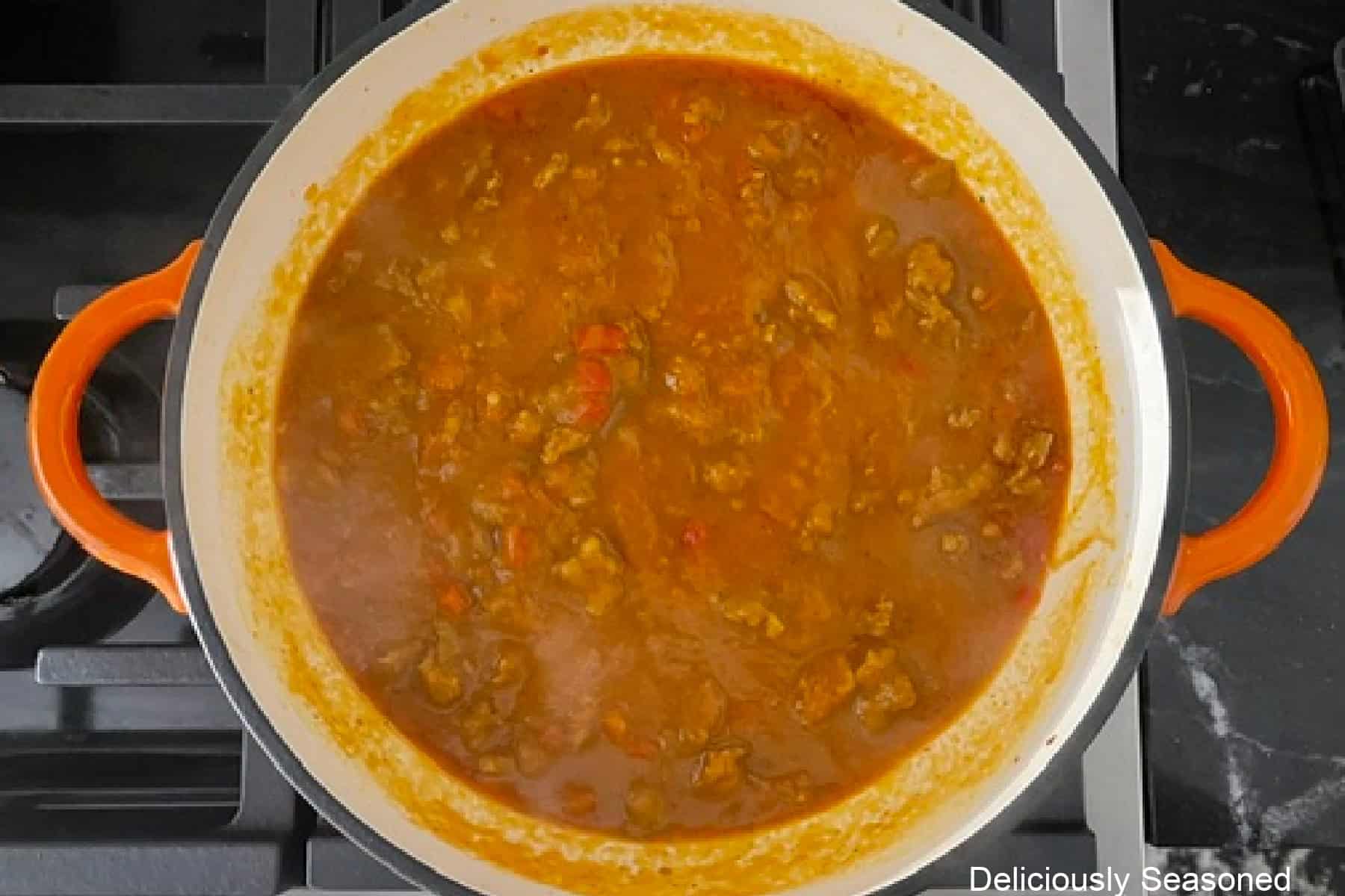 A cast iron pan with a creamy sausage pumpkin sauce simmering on the stove.
