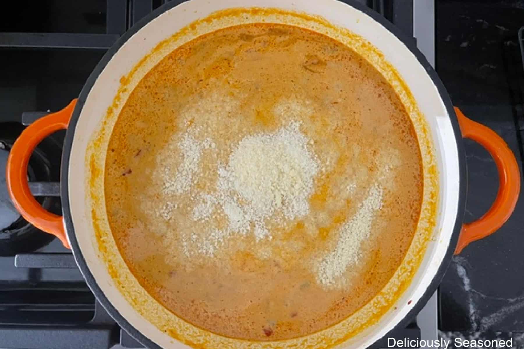 A cast iron pan with grated Parmesan cheese added to the pumpkin sausage sauce.
