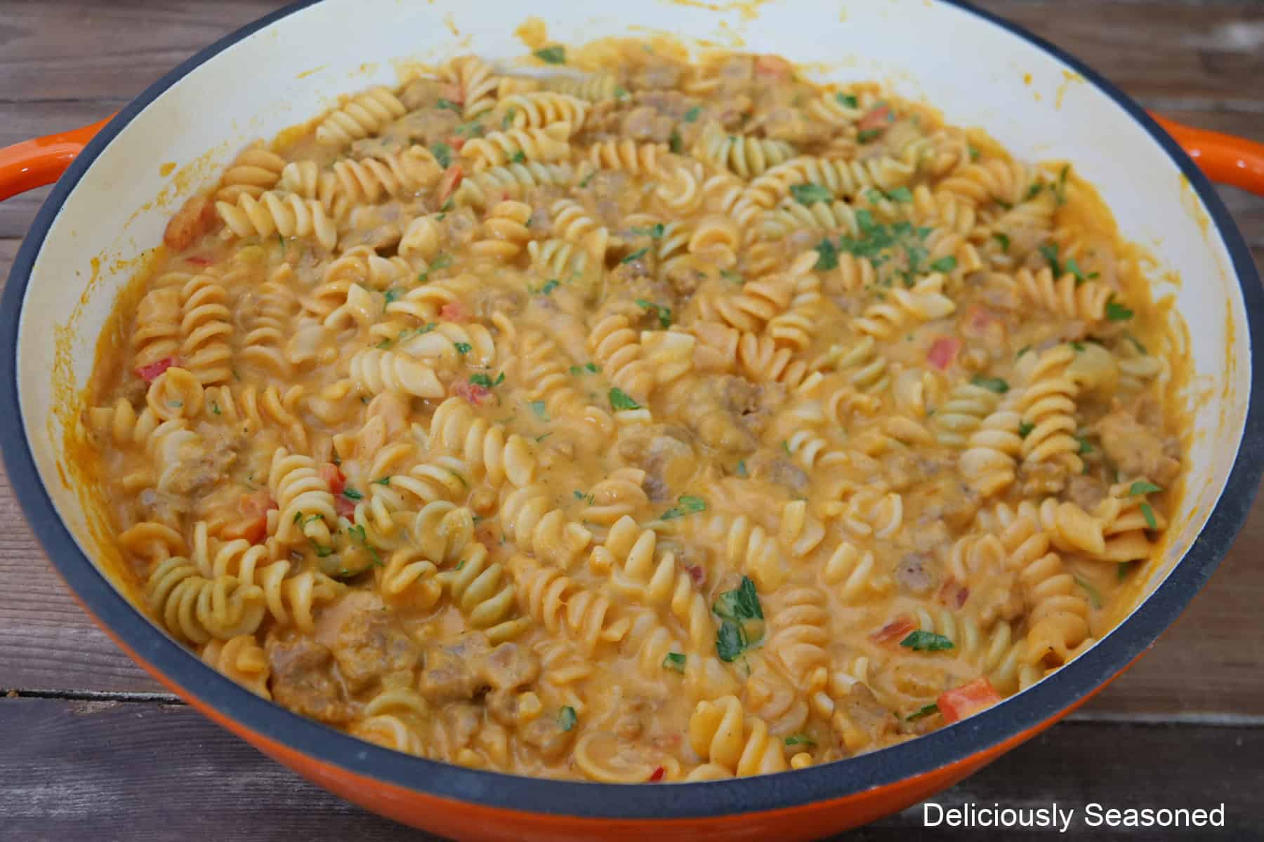 An orange cast iron pan with creamy pumpkin sausage pasta in it after chopped parsley was added.