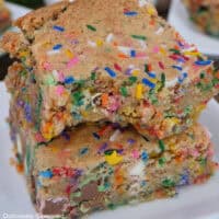 Two funfetti blondies on a white plate with a bite taken out of the blondie on top.