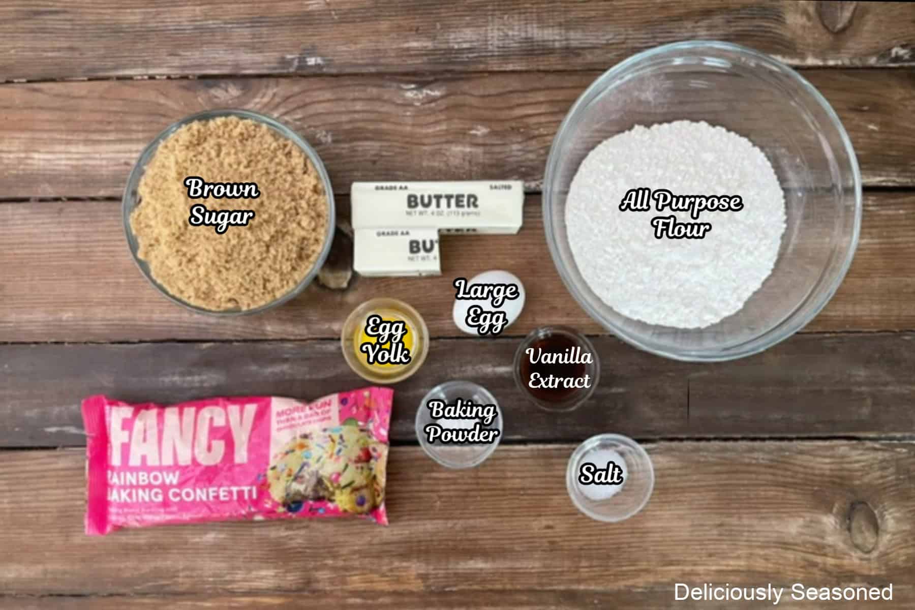 A rustic wood surface with all the ingredients placed on it to make funfetti blondies.
