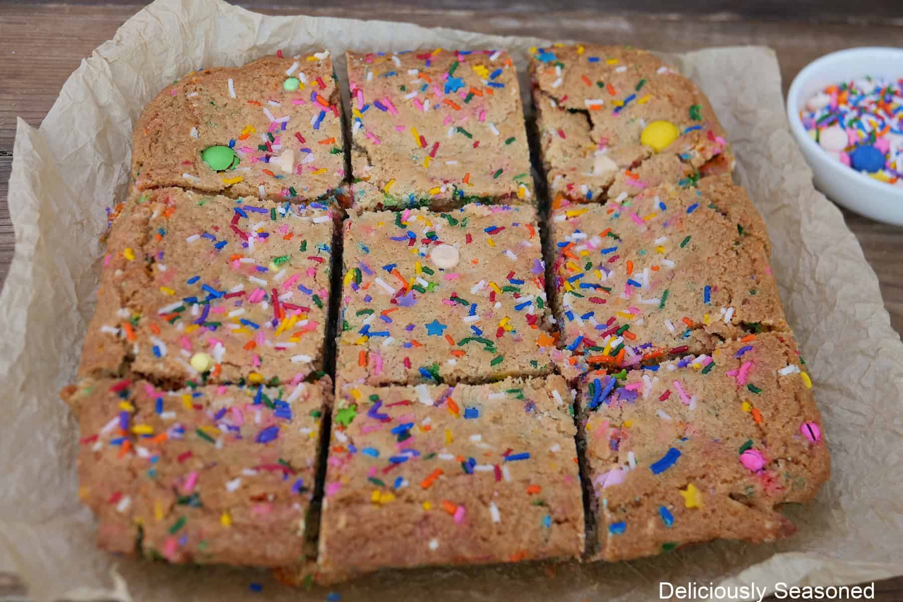 Baked funfetti blondies on parchment paper after being cut into nine servings.
