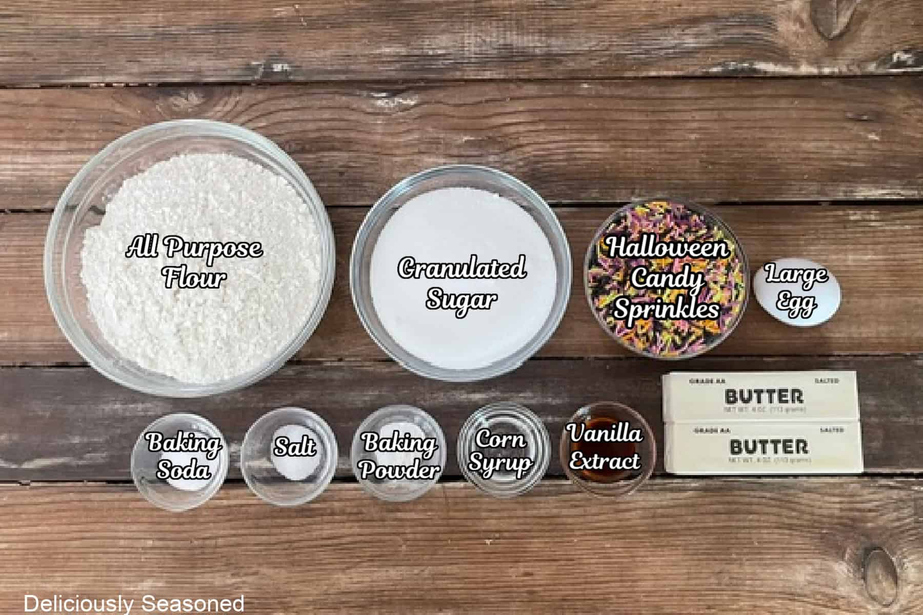 A rustic wood surface with all the ingredients placed on it to make Halloween sugar cookies.