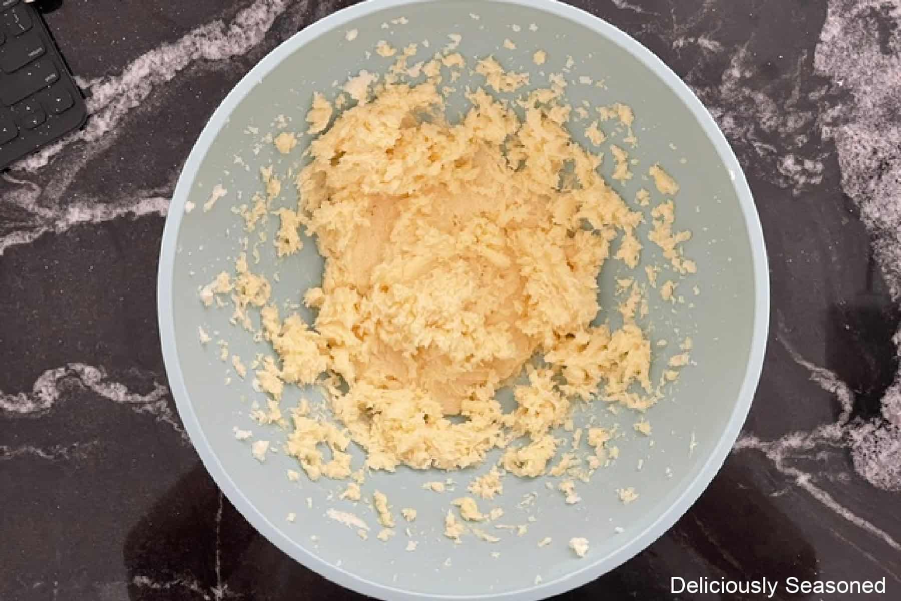 A black granite counter with a light blue bowl filled with sugar cookie dough.