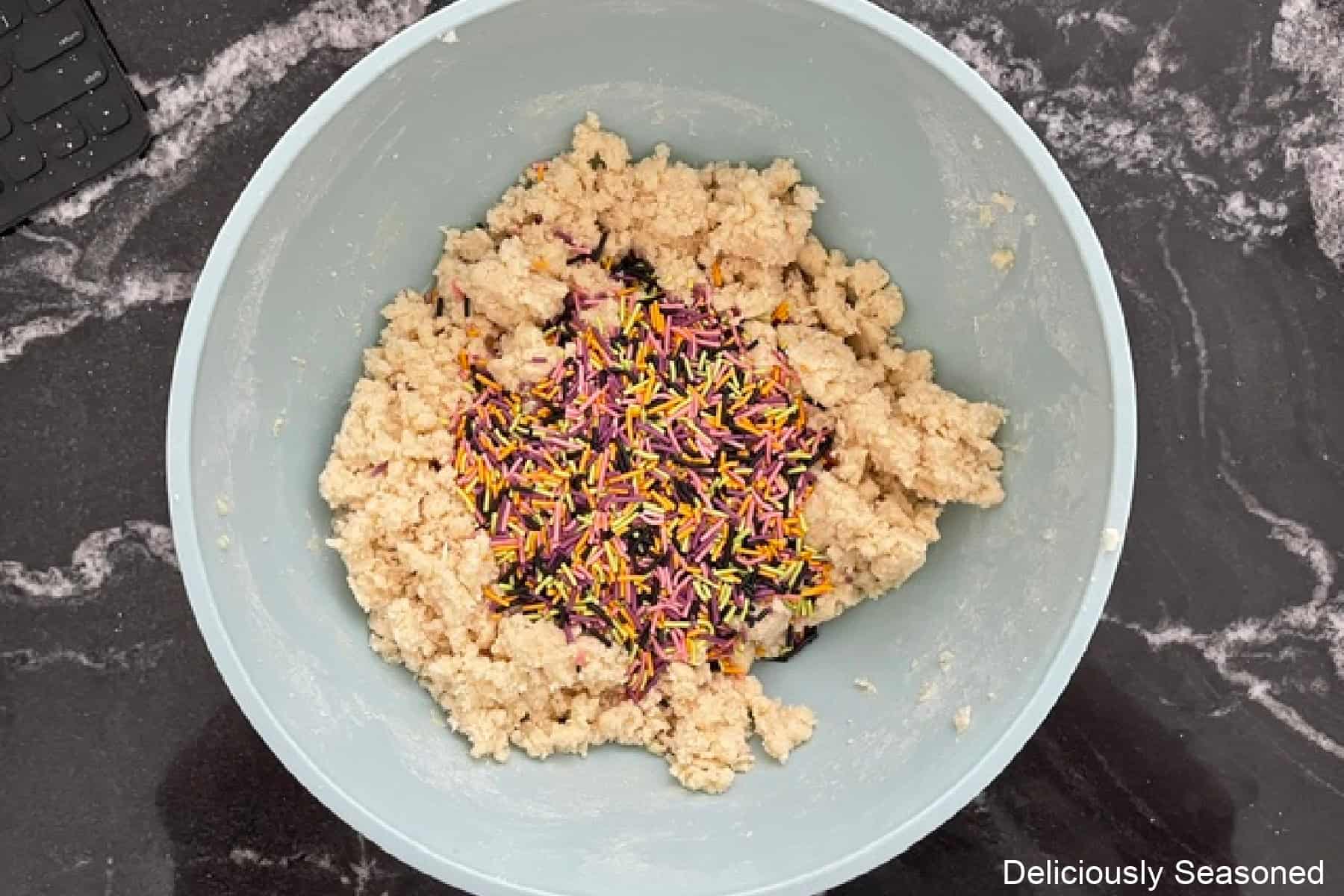 A light blue bowl with sugar cookie dough and Halloween candy sprinkles added to the dough.