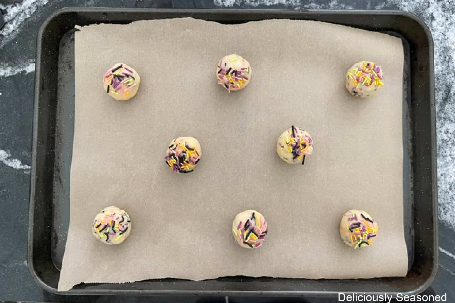 A parchment lined baking sheet with eight sugar cookie dough balls on it before being baked.