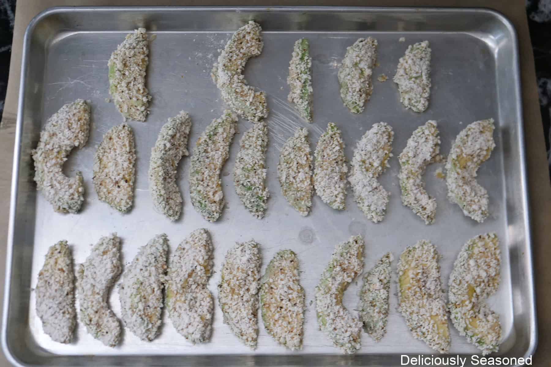 A silver baking sheet with coated avocado fries on it before being deep fried.