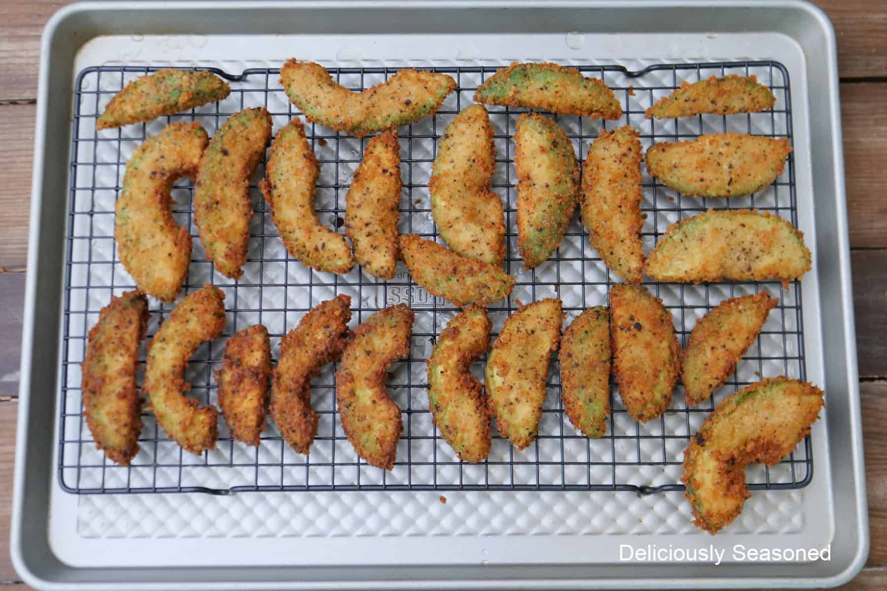 A baking sheet with a wire rack on top with deep fried avocado fries on it.