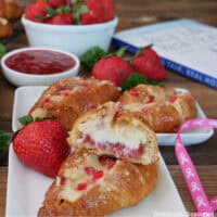 Two white plates with mini strawberry cheesecake croissants on then with fresh strawberries placed randomly around, and a copy of Dr. Loren Rourke's book, Real Talk, Real Hope in the background.