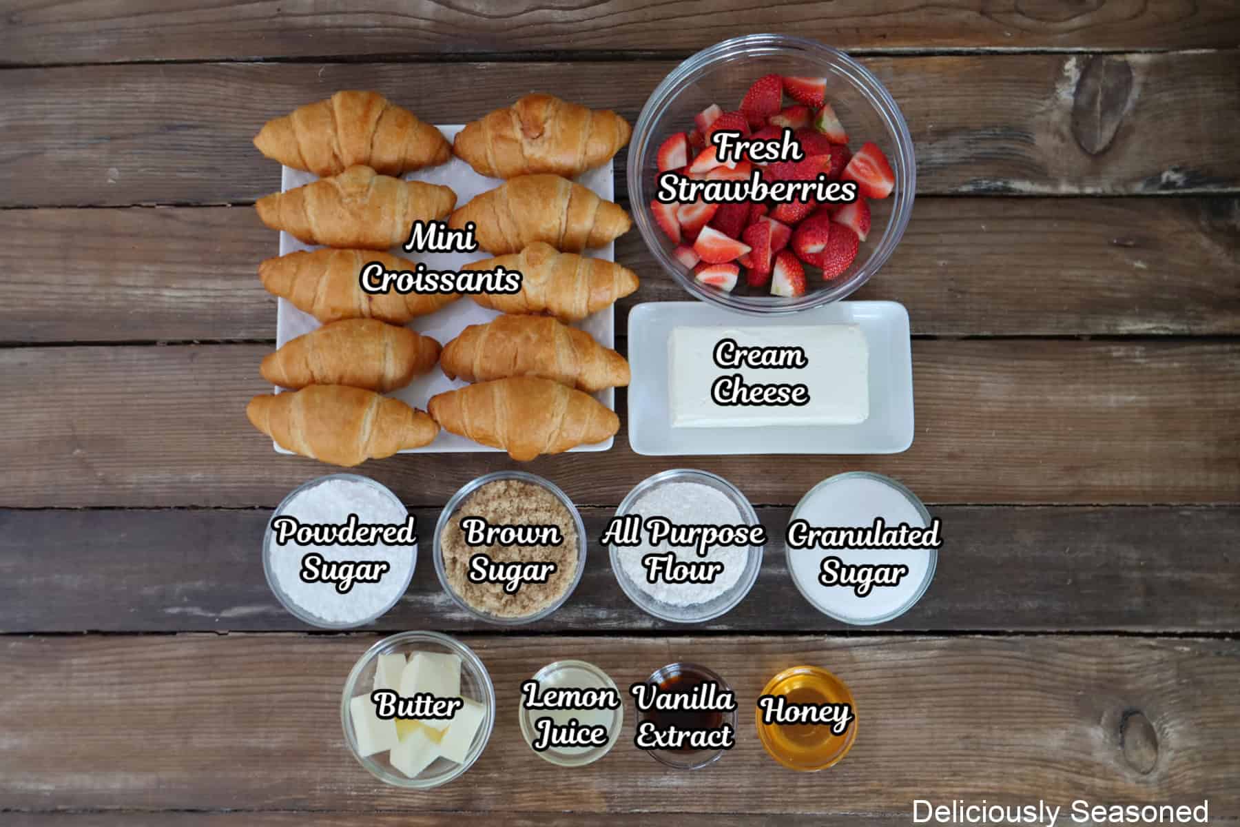 A rustic wood surface with all the ingredients placed on it to make mini strawberry cheesecake croissants.