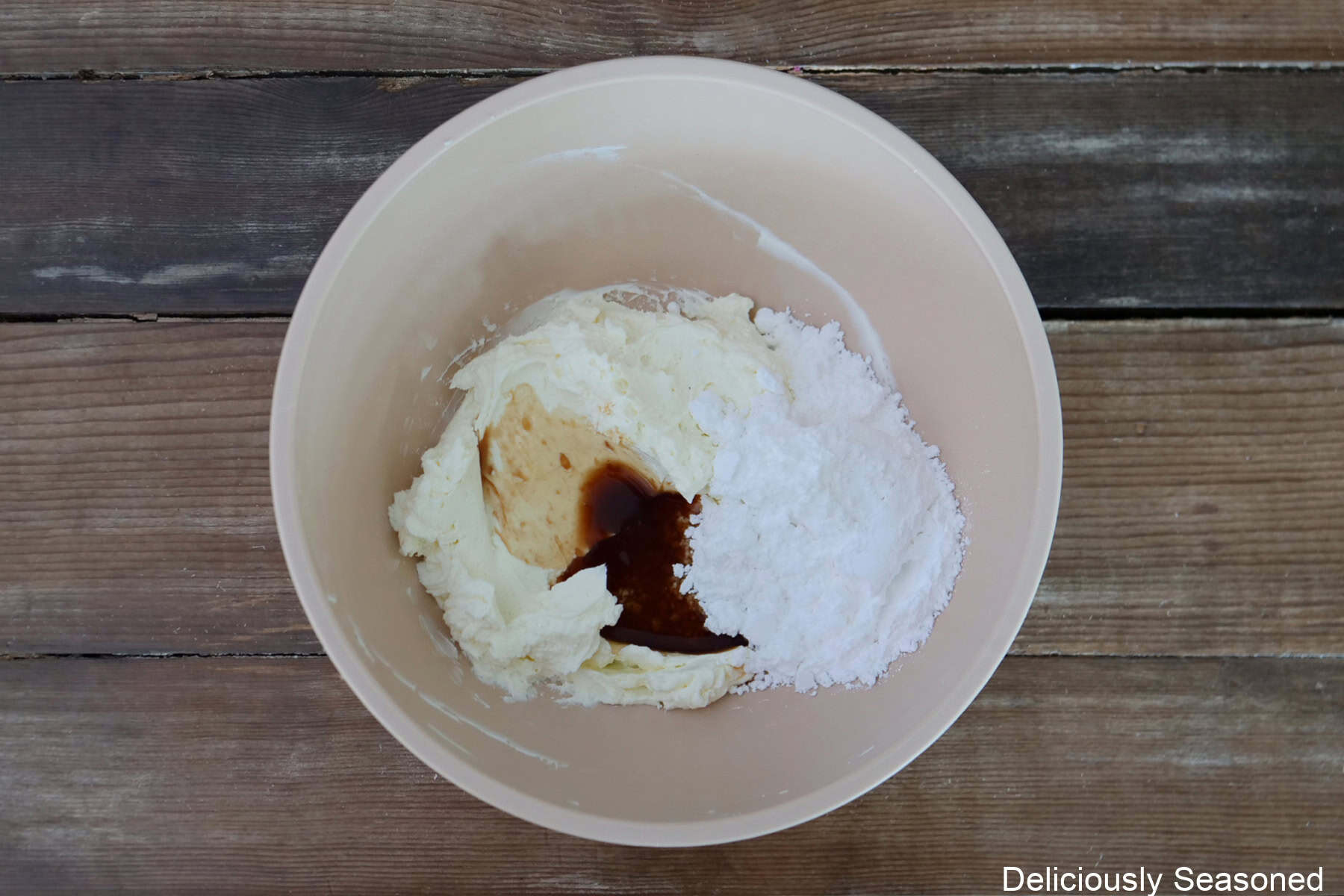 A wood surface with a mixing bowl filled with all the ingredients needed to make cheesecake filling.