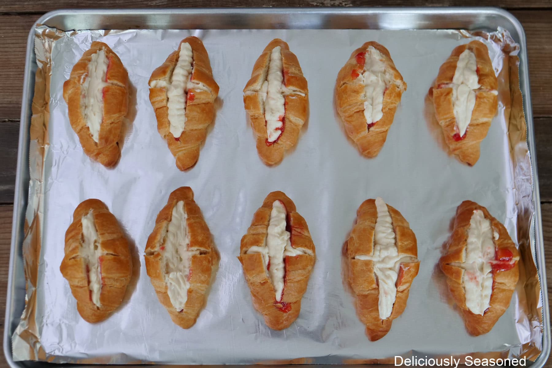 A baking sheet with ten mini croissants placed on it filled with a strawberry filling and sweet cheesecake mixture.