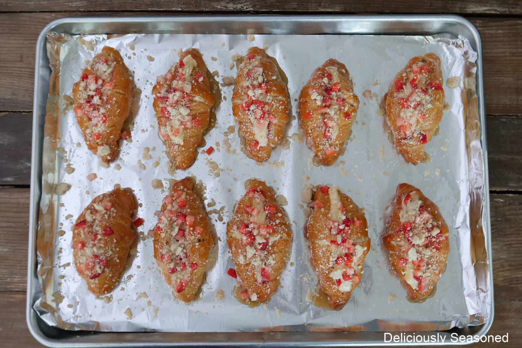 A baking sheet with ten mini strawberry cheesecake croissants on it with the topping and glaze before being baked.