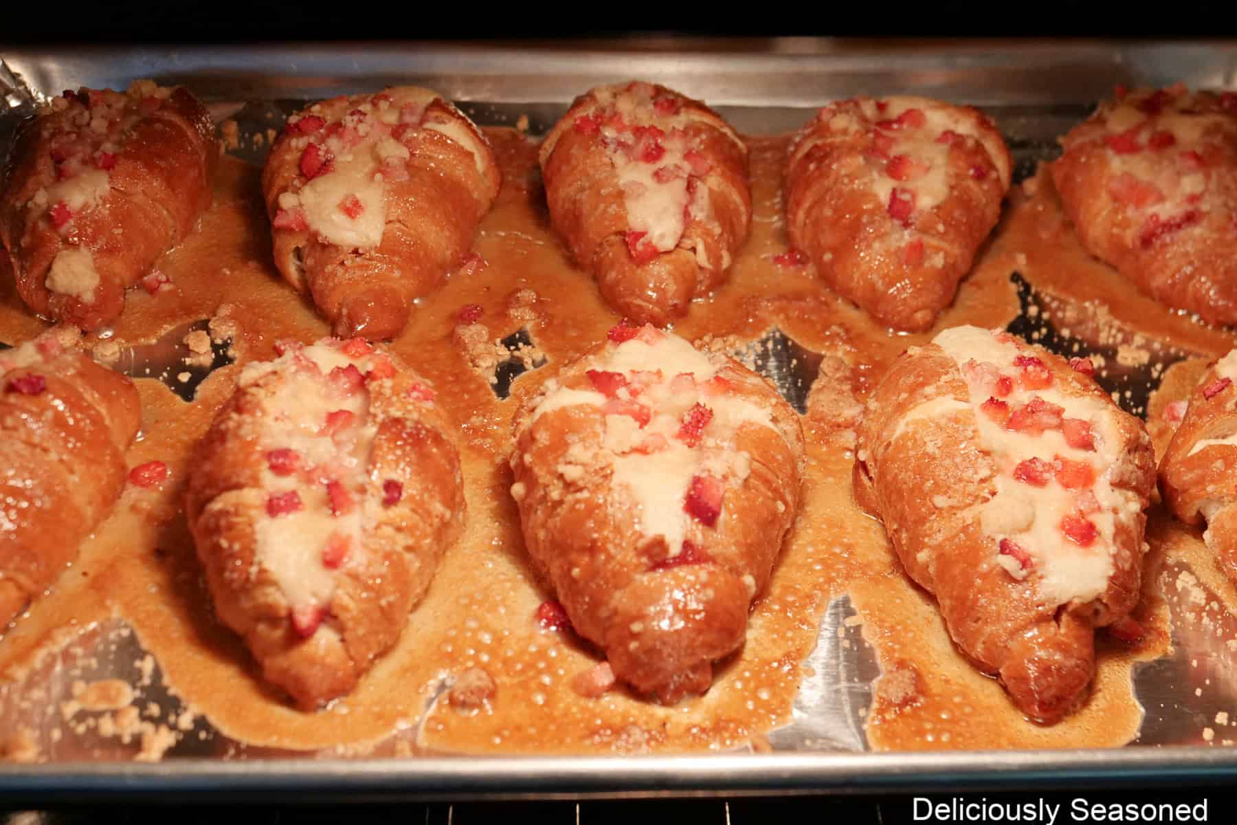A making sheet in the oven with mini strawberry cheesecake croissants on it baking.
