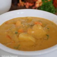 A white bowl filled with pumpkin gnocchi soup with fall foliage in the background.
