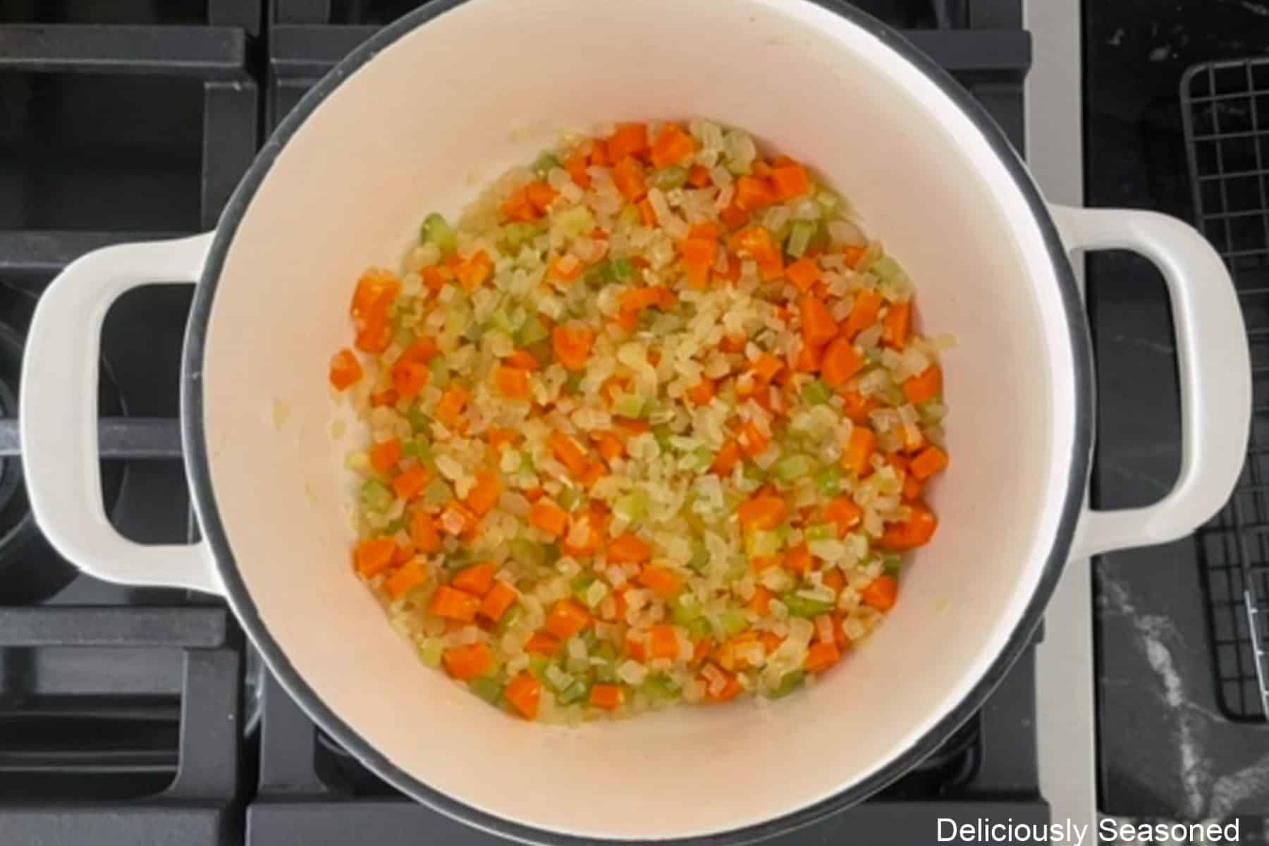 A cast iron pot with sauteed carrot, onions, celery, and garlic in it.