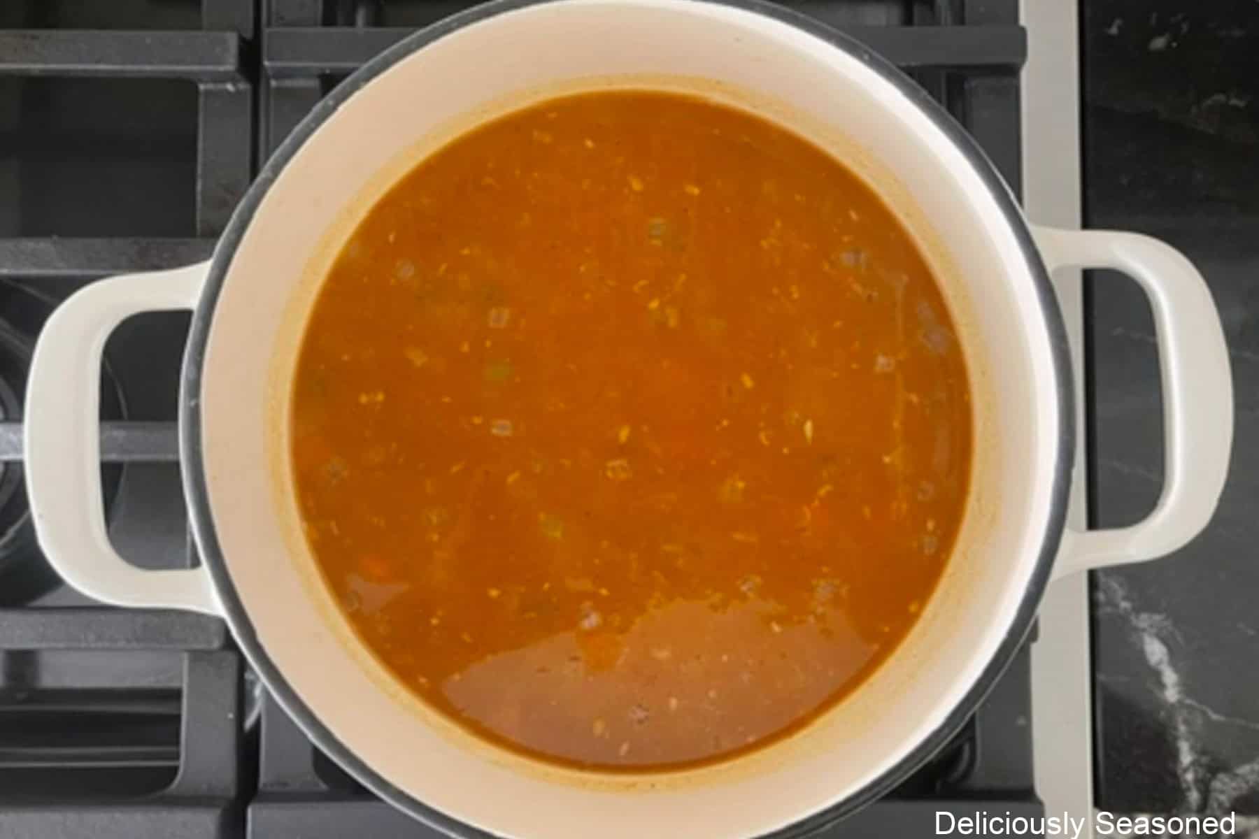 A white cast iron pot with creamy pumpkin added to the broth.