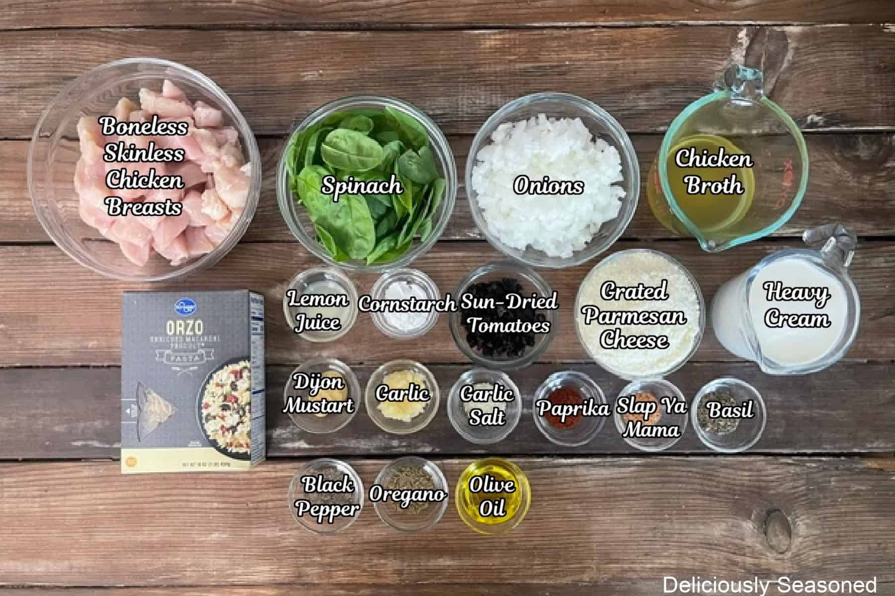A rustic wood surface with all the ingredients placed on it to make Tuscan chicken orzo.