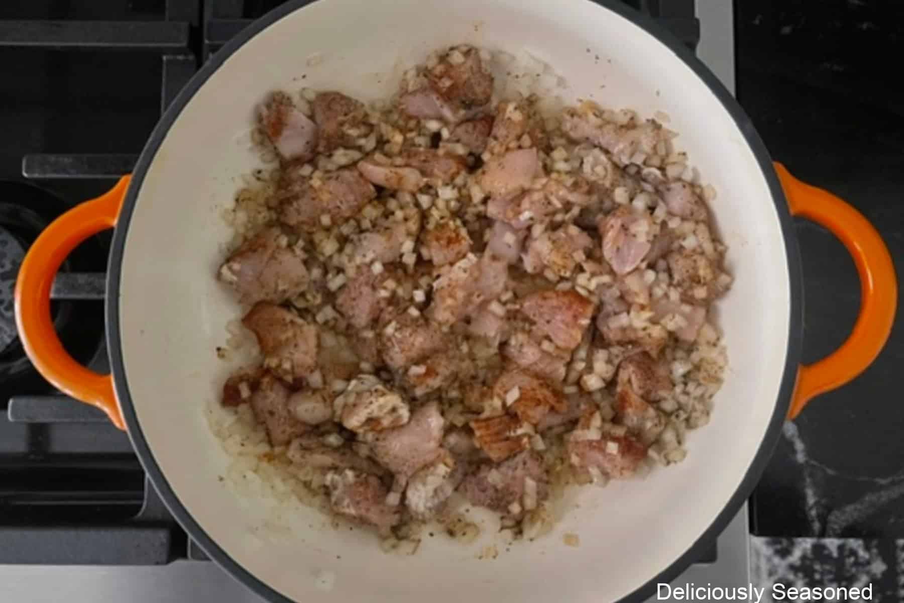 A cast iron pan with minced garlic added to the seasoned chicken mixture.