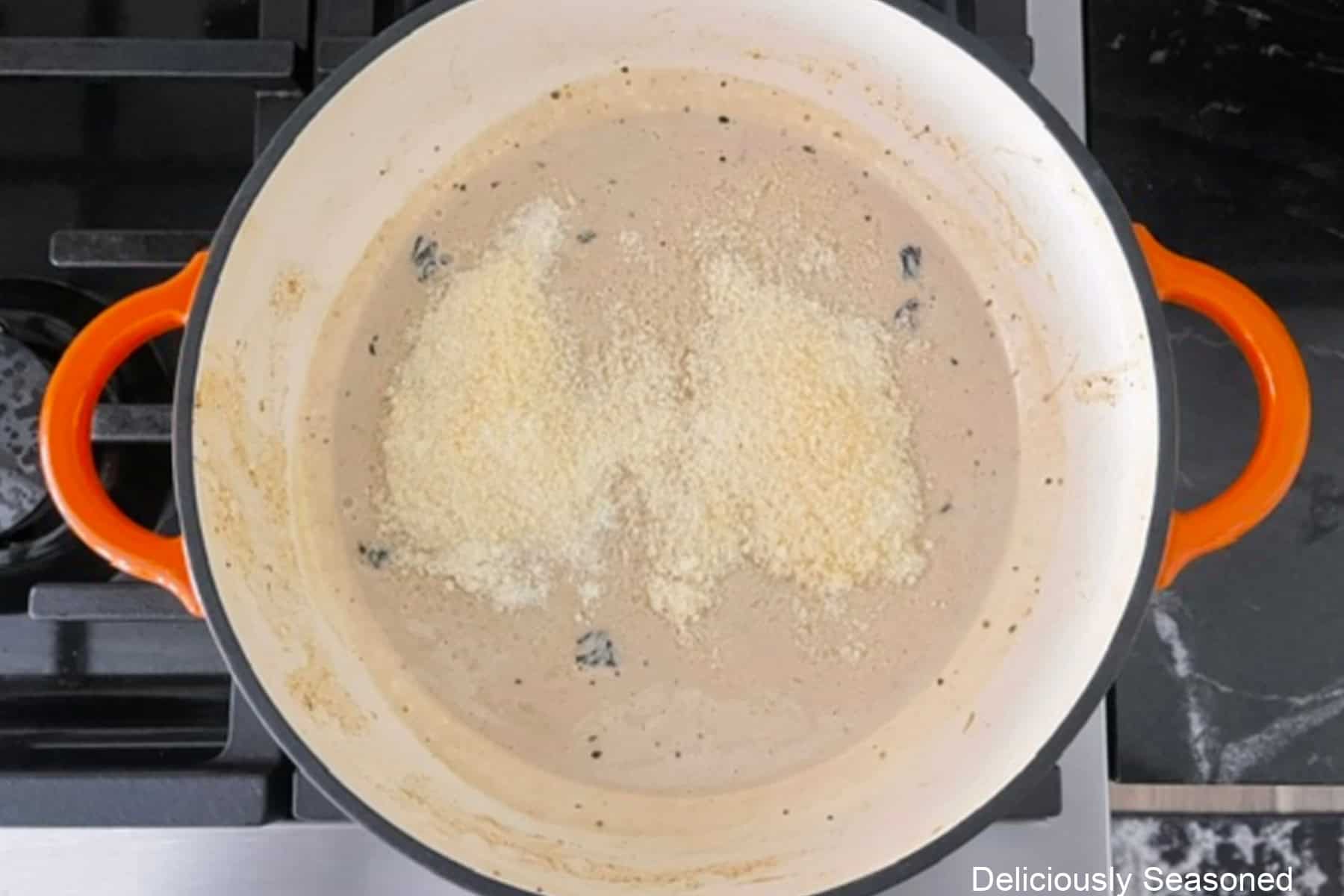 A cast iron pan with a creamy sauce with grated Parmesan added before being stirred into the sauce.