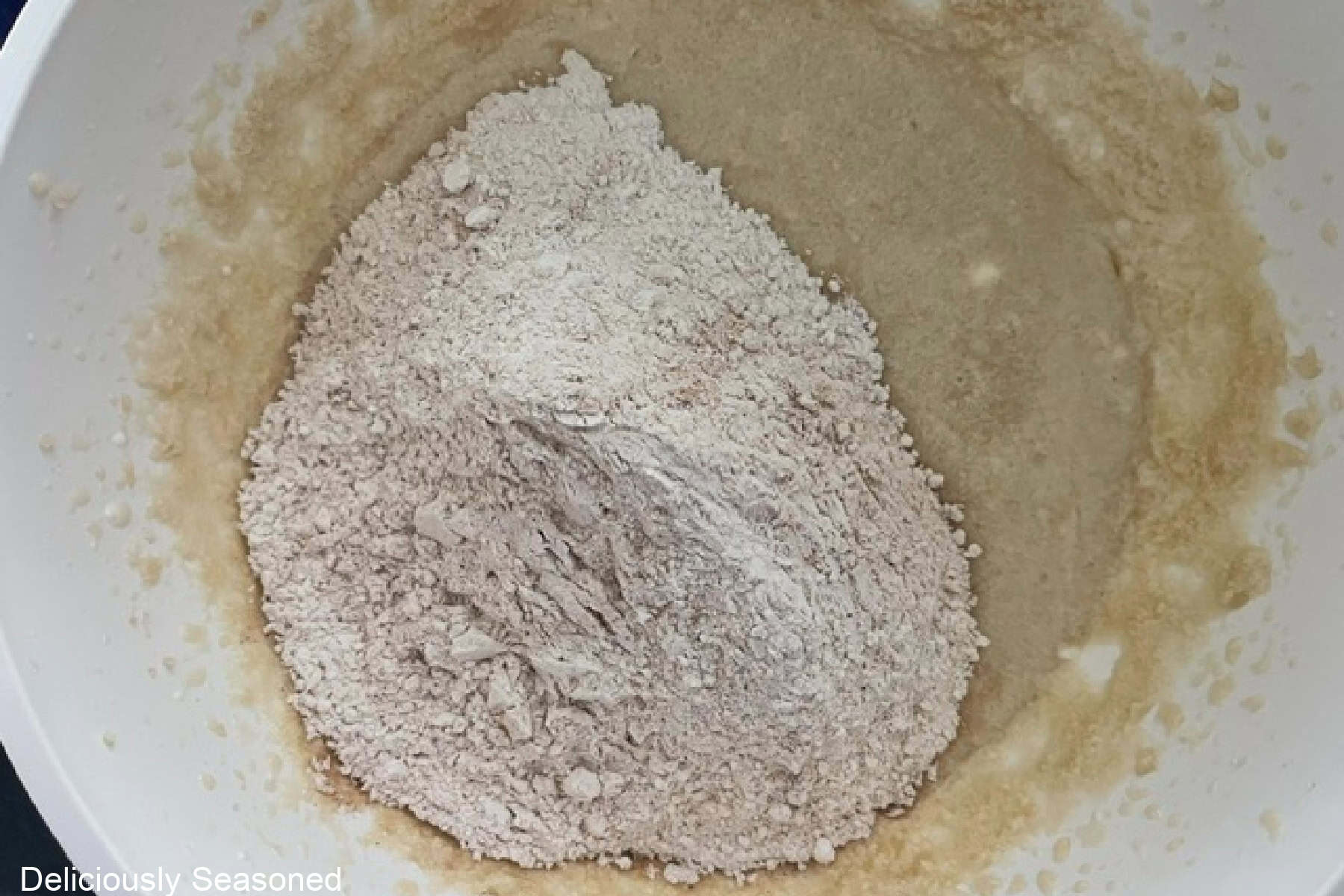 A white bowl with the dry ingredients added to the wet ingredients of the apple coffee cake.
