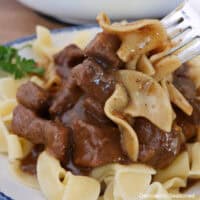 A bowl filled with beef and noodles with a bite on a fork.