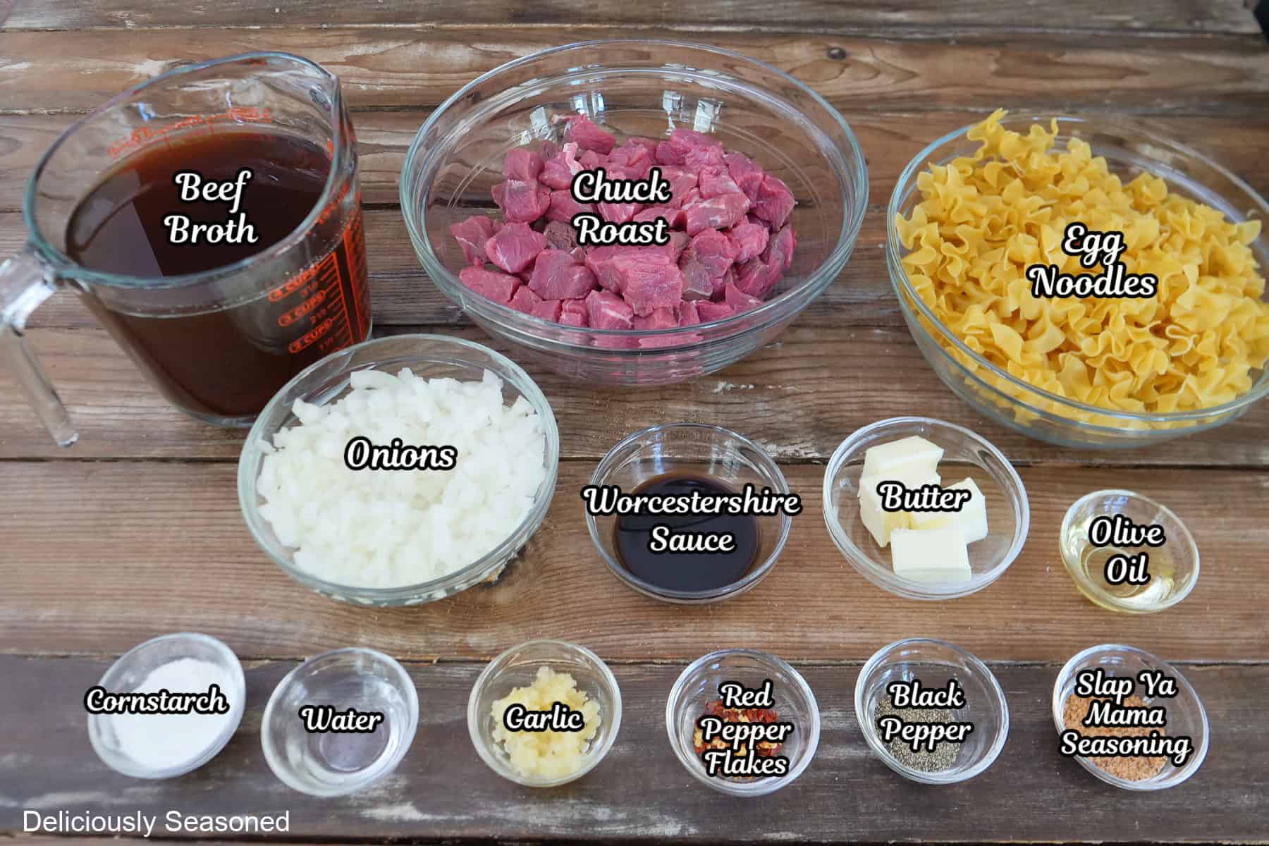 A rustic wood surface with all the ingredients placed on it to make beef and noodles.
